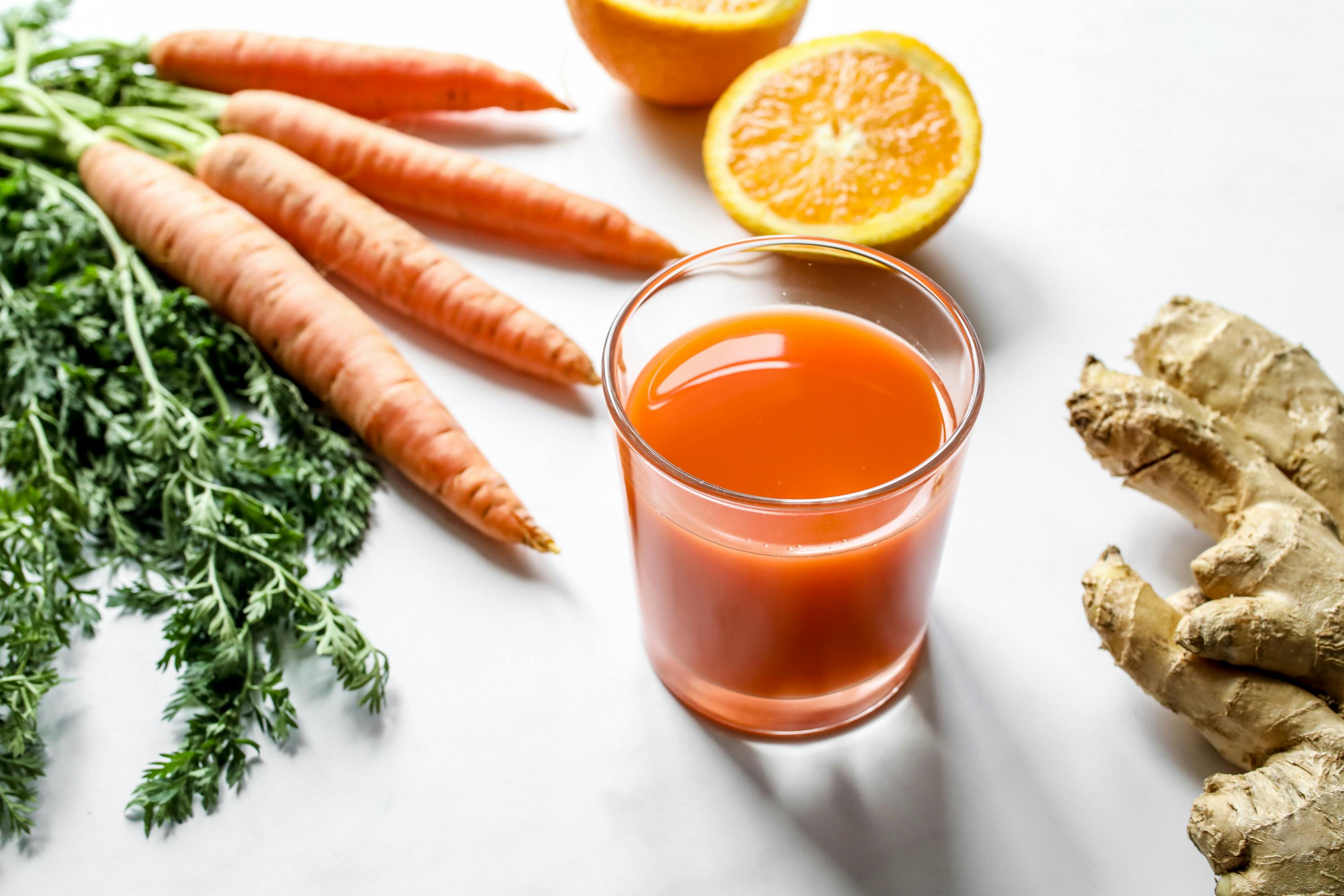 Bright orange sweet potato and carrot juice in a clear glass, styled with fresh ginger and lemon in an overhead flatlay.